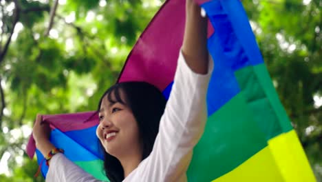 Retrato-de-joven-asiática-ondeando-bandera-lgbt-arco-iris-en-el-parque,-cámara-lenta