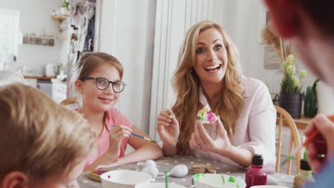 Family-sitting-around-kitchen-table-with-parents-helping-children-to-paint-Easter-decorations---shot-in-slow-motion