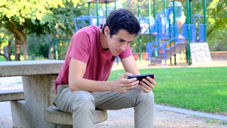 Joven-usando-su-teléfono-inteligente-sentado-en-un-banco-del-parque