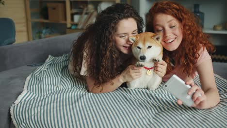 Hermanas-alegres-tomando-selfie-con-adorable-perrito-usando-el-teléfono-inteligente-en-casa