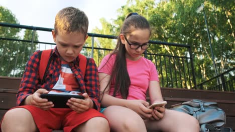 The-older-sister-and-brother-are-sitting-on-the-street,-looking-at-smartphones.