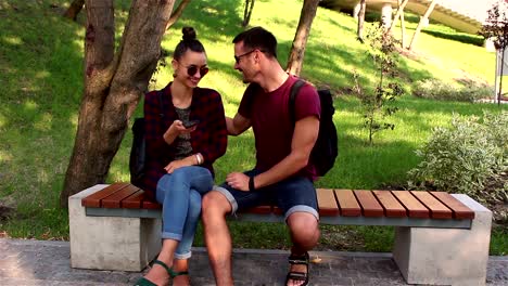 Young-couple-in-love-is-photographed-sitting-on-a-bench-in-the-park.They-are-smiling-and-hugging-each-other.