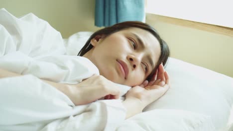 Young-Asian-woman-waking-up-in-the-morning-and-using-smartphone-on-the-bed-room.