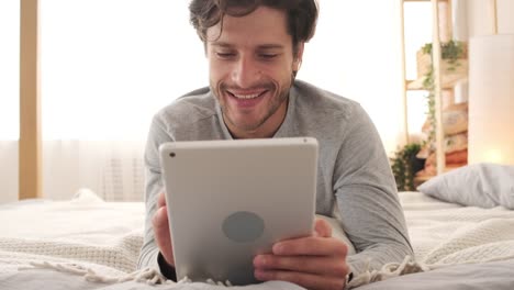 Happy-man-using-digital-tablet-in-bed