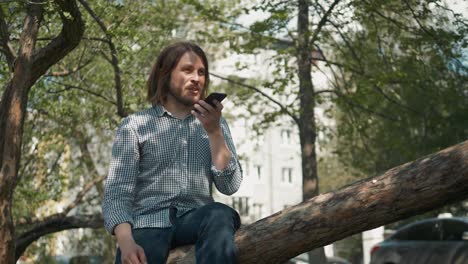 Hipster-man-sending-voice-messages-with-mobile-phone-at-park,-audio-voice-recognition-ai-speech-helper-talk-phone