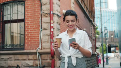 Retrato-de-chica-atractiva-sosteniendo-el-teléfono-inteligente-y-sacar-café-caminando