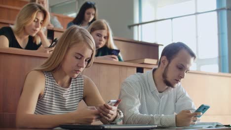 Grupo-multiétnico-de-estudiantes-que-utilizan-teléfonos-inteligentes-durante-la-conferencia.-Jóvenes-que-usan-las-redes-sociales-mientras-estudian-en-la-Universidad.