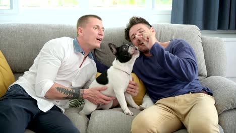 Gay-couple-relaxing-on-couch-with-dog.-Feeding-dog.