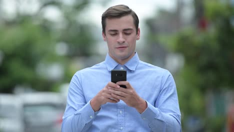 Happy-young-handsome-businessman-using-phone-outdoors