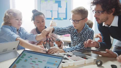 Aula-de-Robótica-de-la-Escuela-Primaria:-Grupo-Diverso-de-Niños-Brillantes-con-Entusiasta-Saqueo-de-Construcción-y-Programación-de-Maestros-Robot.-Diseño-de-software-de-aprendizaje-para-niños-e-ingeniería-de-robótica-creativa