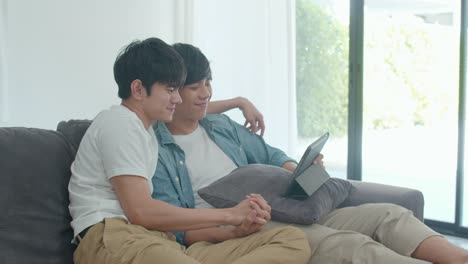 Joven-pareja-Gay-usando-tableta-en-casa.-Los-hombres-LGBTQ-asiáticos-feliz-relajarse-divertido-utilizando-la-tecnología-viendo-películas-en-Internet-juntos-mientras-se-acuesta-sofá-en-el-concepto-de-sala-de-estar.-Disparo-a-cámara-lenta.