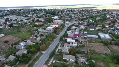 Impresionante-vista-de-pájaro-de-una-carretera-recta-con-coches-en-movimiento-pasando-por-una-ciudad-verde-con-muchos-parques-y-pequeños-edificios-en-verano