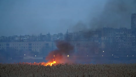 Striking-view-of-the-glowing-cane,-sedge,-and-reed-on-the-Dnipro-riverbank-in-the-suburbs-with-clouds-of-black-smoke.