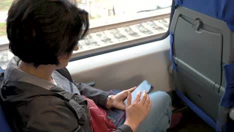 mujer-está-sentada-en-el-tren-sosteniendo-el-teléfono-celular-en-sus-manos-Haciendo-clic-en-la-vista-lateral-trasera