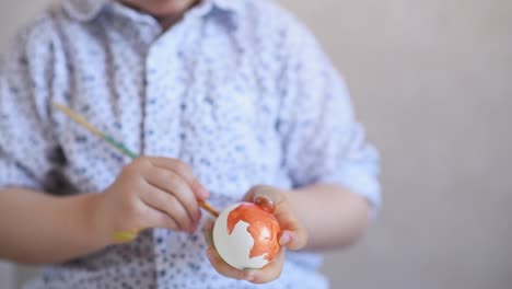 Un-niño-pinta-un-huevo-de-pascua-en-la-mesa-sobre-un-fondo-blanco.