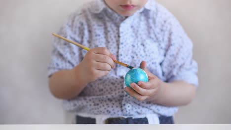 A-little-child-paints-an-one-easter-egg-at-the-table-on-a-white-background.