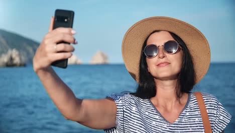 Fröhliche-junge-Frau-posiert-selfie-mit-dem-Smartphone-am-Meer.-Nahaufnahme-auf-4k-RED-Kamera