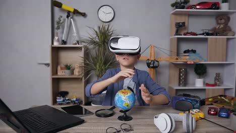 Angenehm-konzentriert-12-alter-interessanter-Junge-arbeiten-mit-kleinen-Globus-mit-speziellen-virtuellen-3D-Brille,-sitzen-in-seinem-Zimmer-am-Tisch