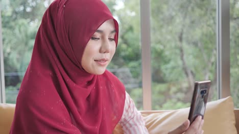 muslimische-Frau-in-traditionellen-Hijab-Kleidung-mit-Smartphone-für-Videoanruf-in-zu-Hause