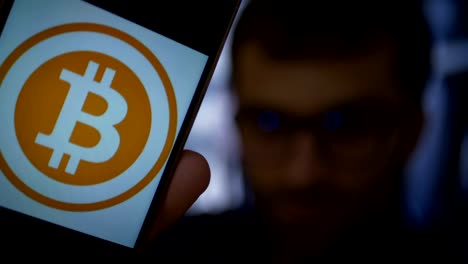 Man-earns-bitcoins-on-his-bitcoin-farm.-Male-making-a-payment-with-bitcoins-cryptocurrency-using-his-smartphone.-Custom-application-interface-design.-Guy-smiles,-earns-on-the-financial-market.