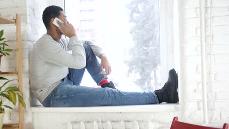 Afro-Amerikaner-Mann-am-Fenster-sitzen-und-telefonieren-mit-Handy