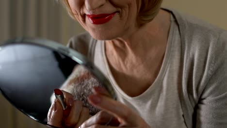 Mature-woman-painting-lips-with-bright-red-lipstick,-remembering-her-young-years