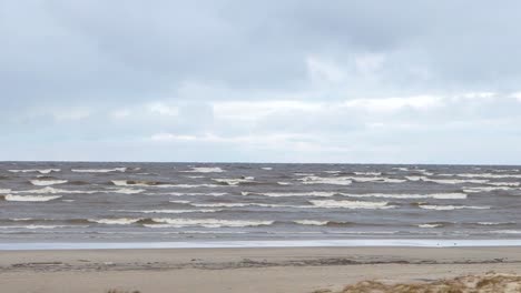 Sea-coastal-waves-rolling-on-empty-sandy-beach,-stormy-cloudy-sunrise-skyview.-Video.-Sea-waves-on-sandy-beach.-Seascape-with-grey-water-on-cloudy-sky.-Power-of-nature.-Wanderlust-or-travelling-and-vacation