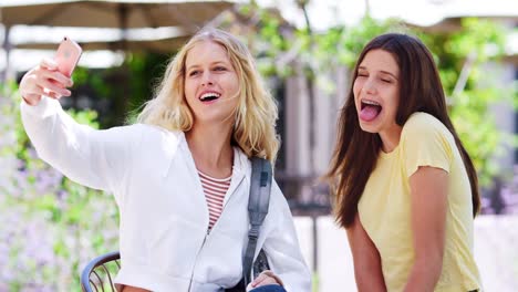 Two-Female-High-School-Students-Posing-For-Selfie-On-Mobile-Phone-Outside-College-Buildings