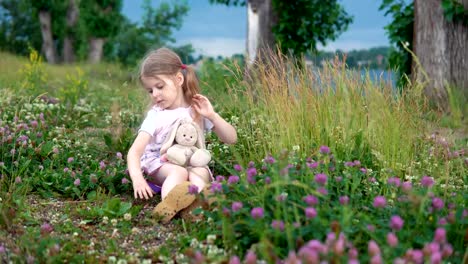 Ein-kleines-Mädchen-spielen-mit-einem-Spielzeug-Hasen-auf-der-Wiese-unter-den-blühenden-Klee