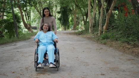 Mujer-mayor-con-su-hija-empujando-la-silla-de-ruedas-por-el-Parque