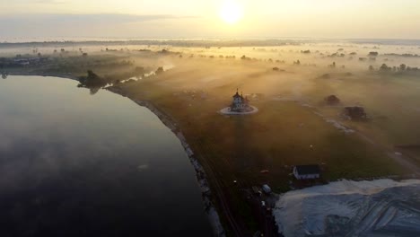 Luftaufnahmen-Video-der-kleinen-Dorfkirche-am-nebligen-Morgen.-Sonnenaufgangszeit.-Kyiv-Region,-Ukraine.-Fliegen-über-den-Fluss-Desna