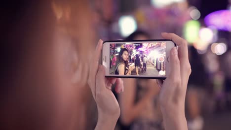 Traveler-backpacker-blogger-Asian-women-lesbian-lgbt-couple-travel-using-smartphone-takes-photos-in-Thailand.-Female-drinking-alcohol-or-beer-at-Khao-San-Road-the-most-famous-street-in-Bangkok.