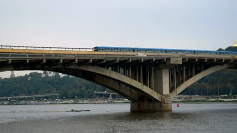 Train-travels-over-the-bridge-against-the-sky-and-the-domes-of-the-church.-City-subway-left-outside.-Public-transport-on-the-move.-Cars-go-over-the-bridge-over-the-river.