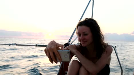 Young-woman-sails-yacht-and-uses-a-smartphone---takes-a-selfie