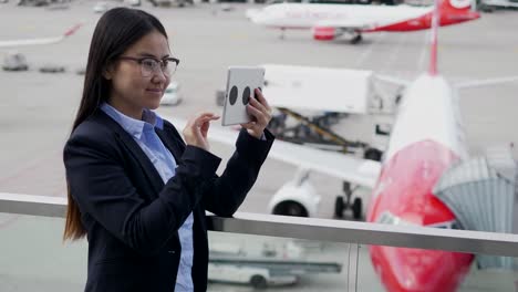 Happy-Asian-lady-communicating-by-text-messaging-on-tablet-at-airport