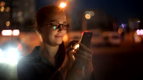 Porträt-der-jungen-schönen-kaukasischen-Frau-mit-Smart-Phone-Hand-halten-im-Freien-in-der-Stadtnacht,-lächelnd,-Gesicht-beleuchteten-Bildschirmlicht-soziales-Netzwerk,-Technologie,-Kommunikation-Konzept