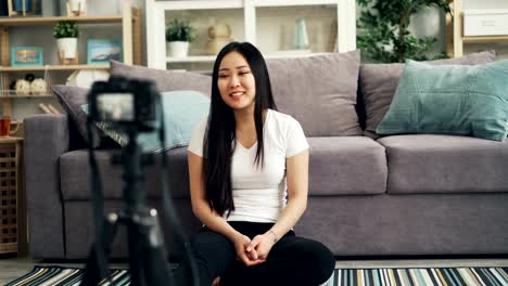 Cute-Asian-girl-female-blogger-is-recording-video-for-her-internet-vlog-looking-at-camera-and-talking-smiling-and-laughing.-Blogging-and-technology-concept.