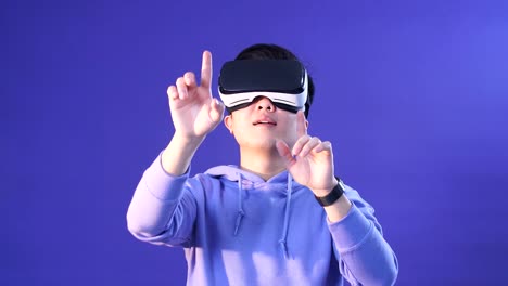 Joyful-Japanese-youngster-playing-videogame-in-virtual-reality-helmet-on-dark-blue-background