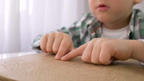 Schule-der-blinden-Kinder,-erkrankter-kleiner-Junge,-der-Braille-Buch-mit-Zeichen-Schrift-für-Sehbehinderte-am-Tisch-sitzt