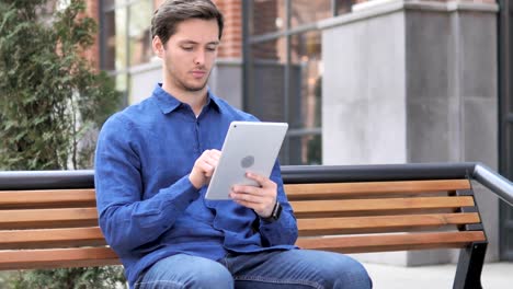 Junger-Mann-nutzt-Tablet-beim-Sitzen-auf-Bank