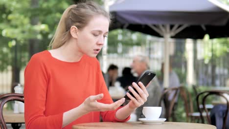 Young-Woman-Upset-by-Loss-on-Smartphone,-Sitting-in-Cafe-Terrace