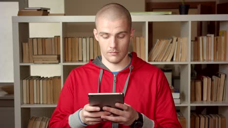 Retrato-de-primer-plano-de-joven-atractivo-estudiante-masculino-caucásico-usando-la-tableta-en-la-biblioteca-de-la-universidad-en-interiores