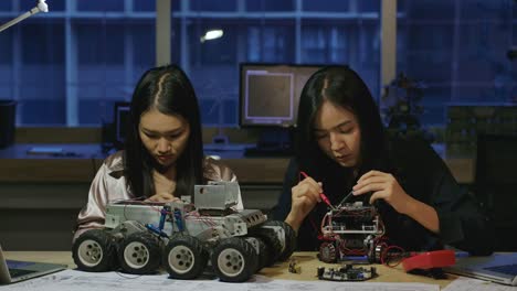 Team-of-young-electronics-development-engineers-building,-testing,-fixing-robotics-prototype-at-night-in-laboratory.-People-with-technology-or-innovation-concept.