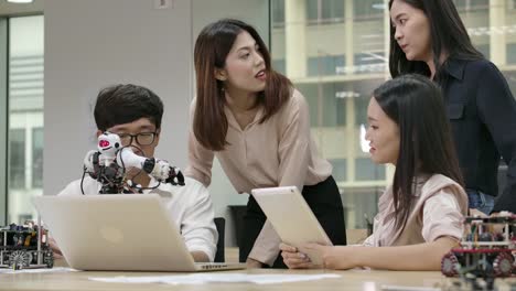 Young-asian-creative-engineers-meeting,-programming-for-collaborative-universal-robotics-at-laptop-in-workshop.-People-with-technology-or-innovation-concept.