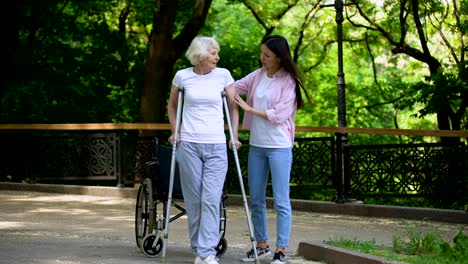 Mujer-joven-ayudando-a-la-anciana-caminando-con-muletas,-rehabilitación-de-fractura-de-cadera