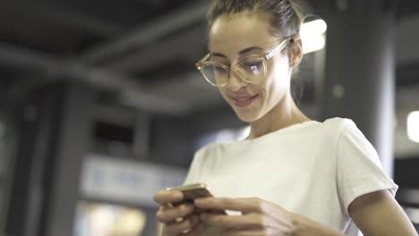 joven-sonriendo-elegante-mujer-hermosa-en-camiseta-blanca-y-gafas-transparentes-está-utilizando-teléfono-inteligente-al-aire-libre.-mujer-buscando-algo,-escrutando-las-redes-sociales,-chateando-y-enviando-mensajes-de-texto