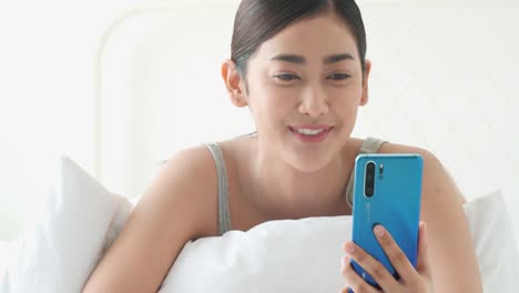 Asiatische-Frau-sprechen-in-Echtzeit-mit-Smartphone-im-Bett-Zimmer.-Konzept-von-Technologie,-Kommunikation-und-Social-Media.