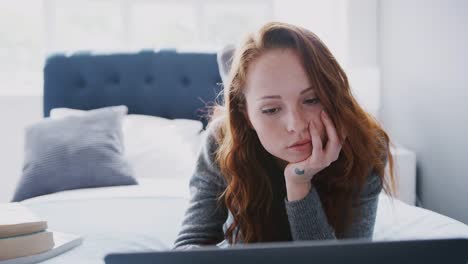 Female-college-student-lying-on-bed-wearing-working-on-laptop---shot-in-slow-motion