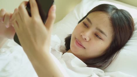 Junge-asiatische-Frau-aufwachen-am-Morgen-und-mit-dem-Smartphone-auf-dem-Schlafzimmer.