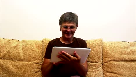 Eine-attraktive-erwachsene-Frau-ist-Video-Chat-mit-ihrer-Familie,-auf-einem-Tablet-PC,-sitzen-auf-einem-Sofa-zu-Hause.